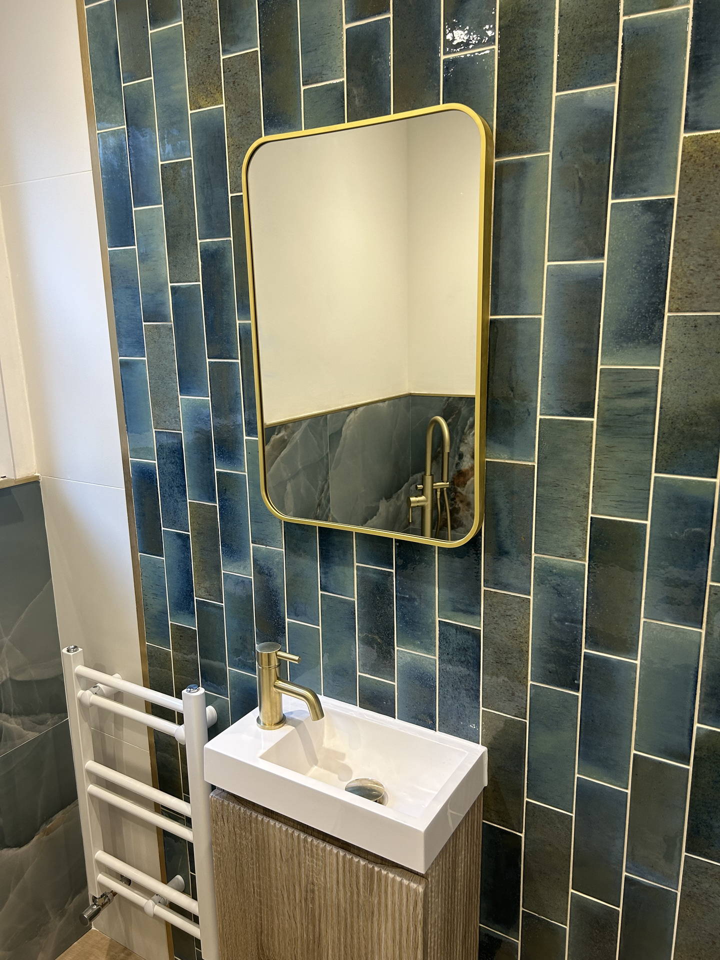 Close on the cloakroom wet wall: the green tile in vertical stacks with a brass line at every edge, the brass-framed mirror and the fluted vanity with its brass tap.