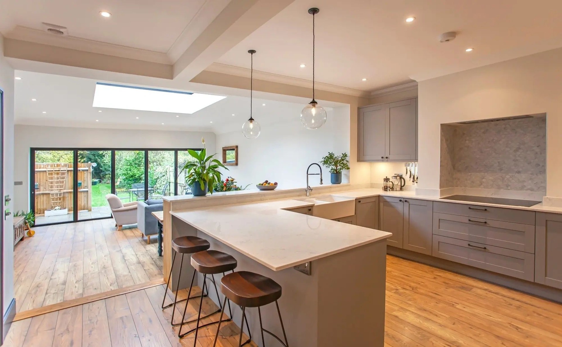 A kitchen extension: grey shaker units around an island with stools, a roof light above and bifold doors open to the garden.