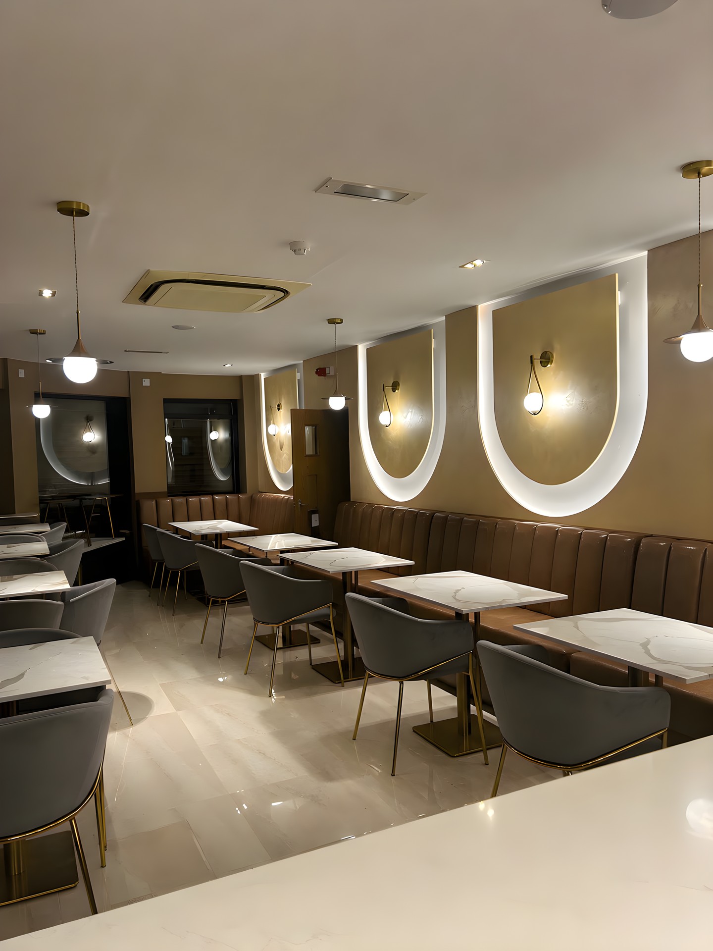 The Kashmiri Karahi dining room in Slough: three arched recesses lit from within, brass wall lights, a fluted tan leather banquette and stone-topped tables.