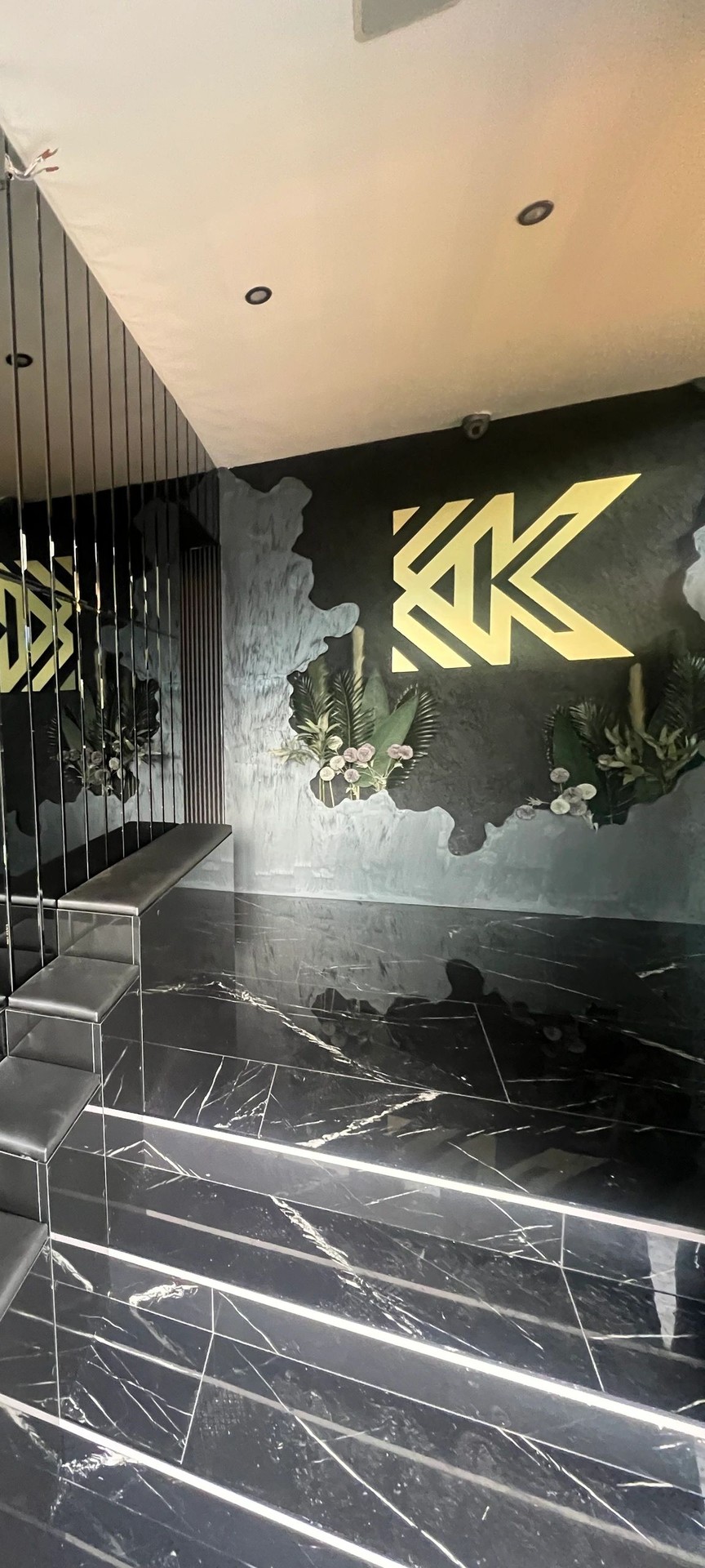 Front of house at Kashmiri Karahi: the gold KK monogram on a stone-effect wall above a black marble floor with lit strip lines, and a mirror wall to one side.
