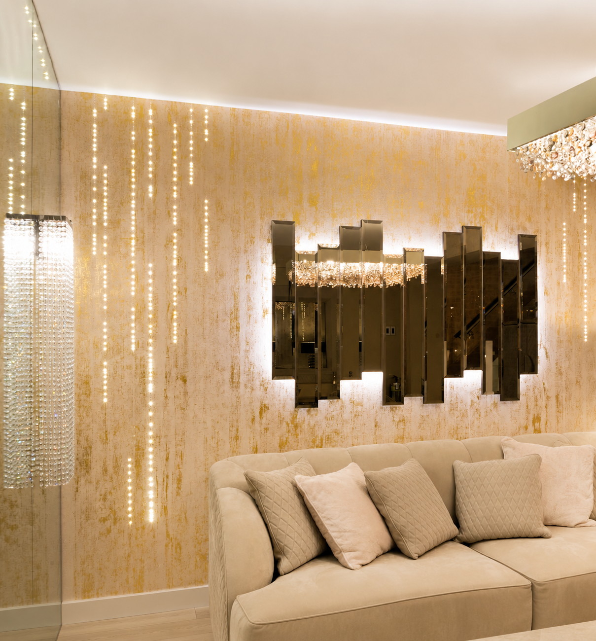 A lounge: bevelled bronze mirror panels lit from behind on a wall of gold leaf, a crystal chandelier, strands of crystal at the window and a cream sofa.