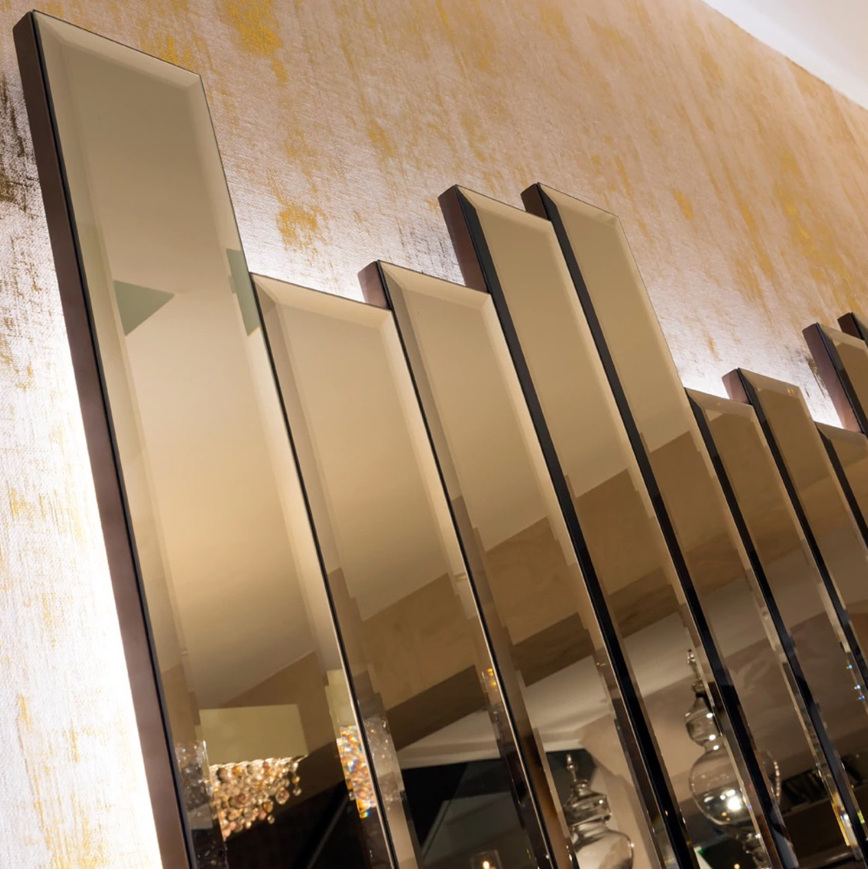 Close on the mirror wall: the bevelled edges of the bronze panels and the light behind them, with the chandelier caught in the glass.